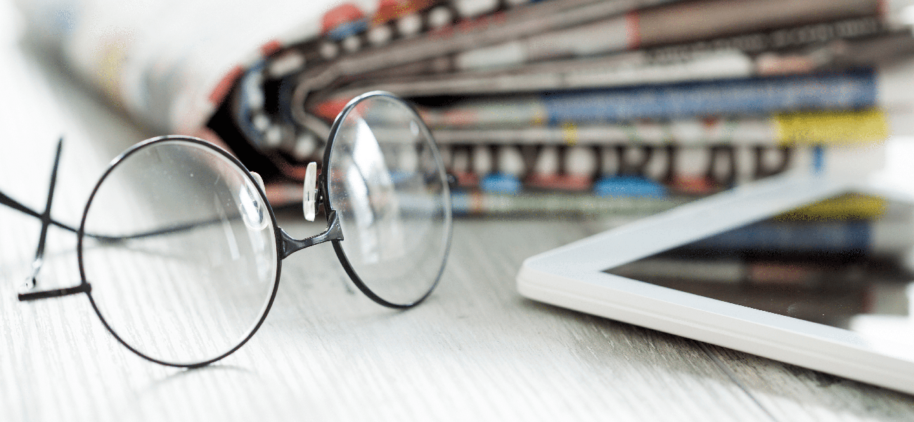 A pair of reading glasses next to a tablet and a newspaper.