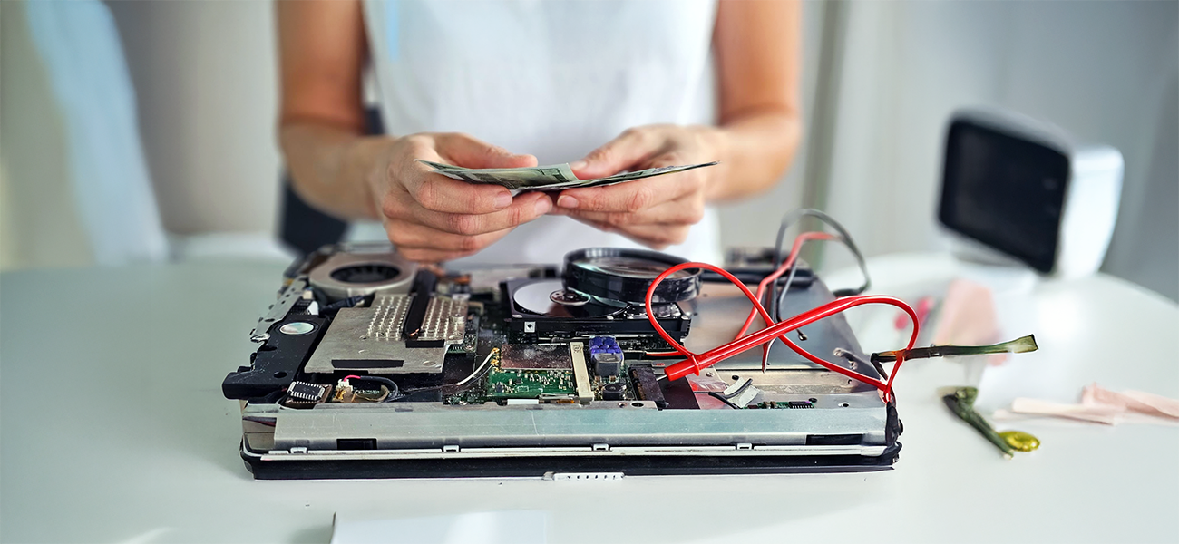 Image: District administrator counting repair costs over a dismantled laptop.