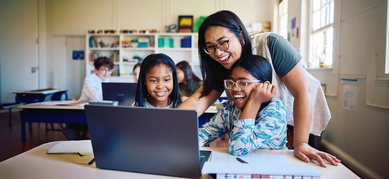 Header image: A teacher assisting students on a laptop in class.