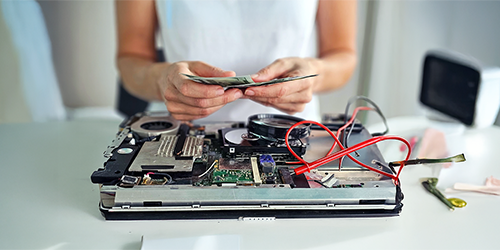 Image: District administrator counting repair costs over a dismantled laptop.
